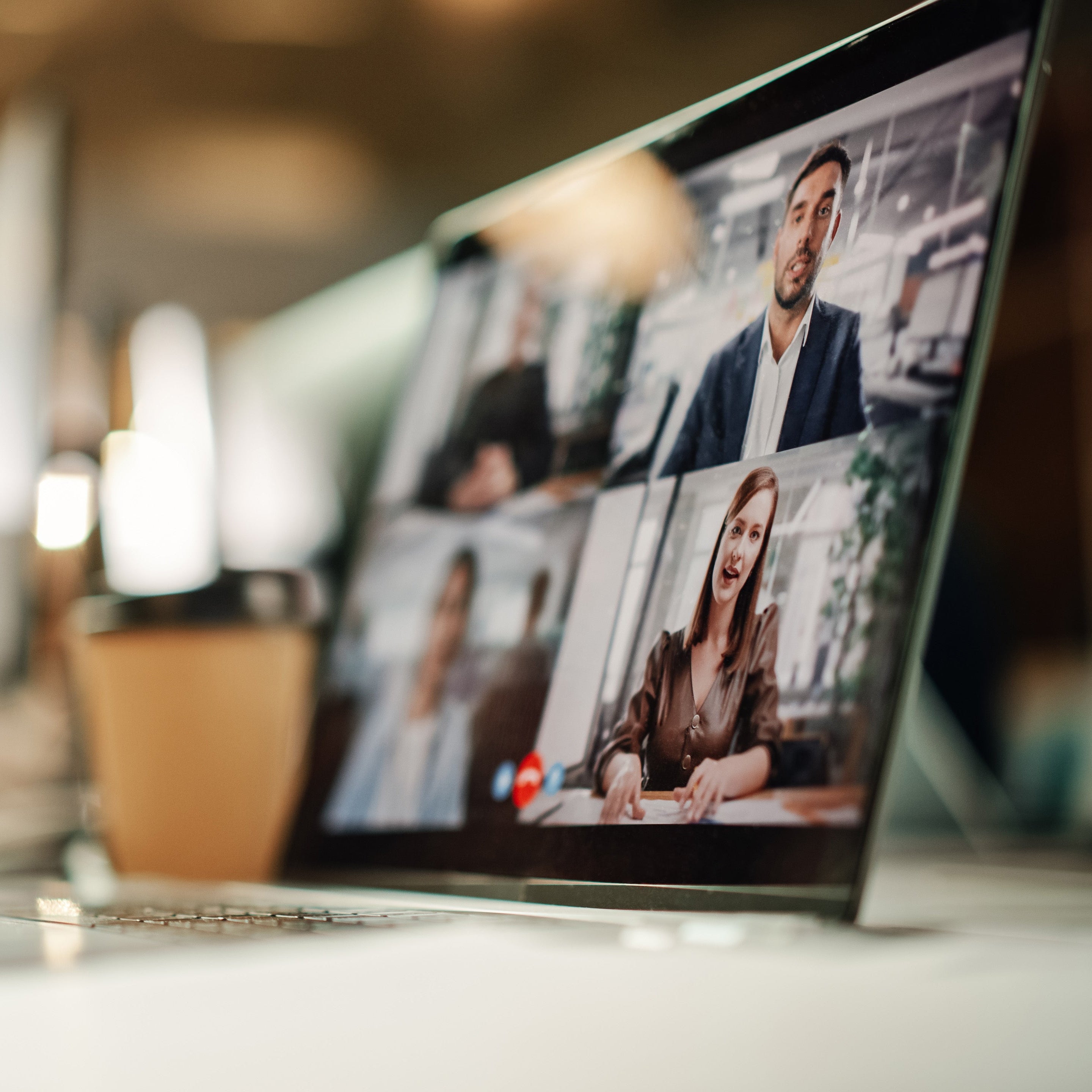 Person using a laptop for a video call with multiple people in an indoor setting.